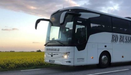 En vit buss från företaget BD Bussresor som åker på en landsväg, längst en gul äng.